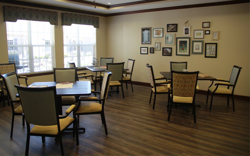 A cozy dining area with multiple tables and chairs, decorated with wall art and large windows for natural light.