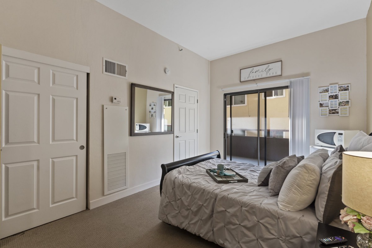 A well-appointed bedroom with a bed, mirror, and sliding glass doors leading to a balcony.