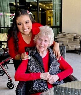 A young woman and an elderly woman smiling together outdoors.