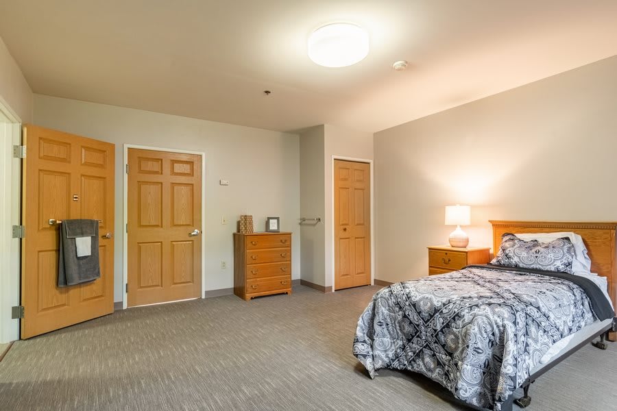 A spacious bedroom with a bed, dresser, and lamp.