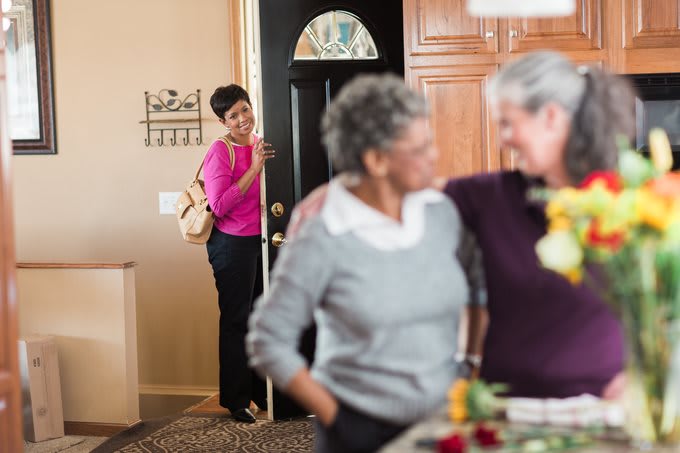 A person arrives at a home, greeted warmly by friends.