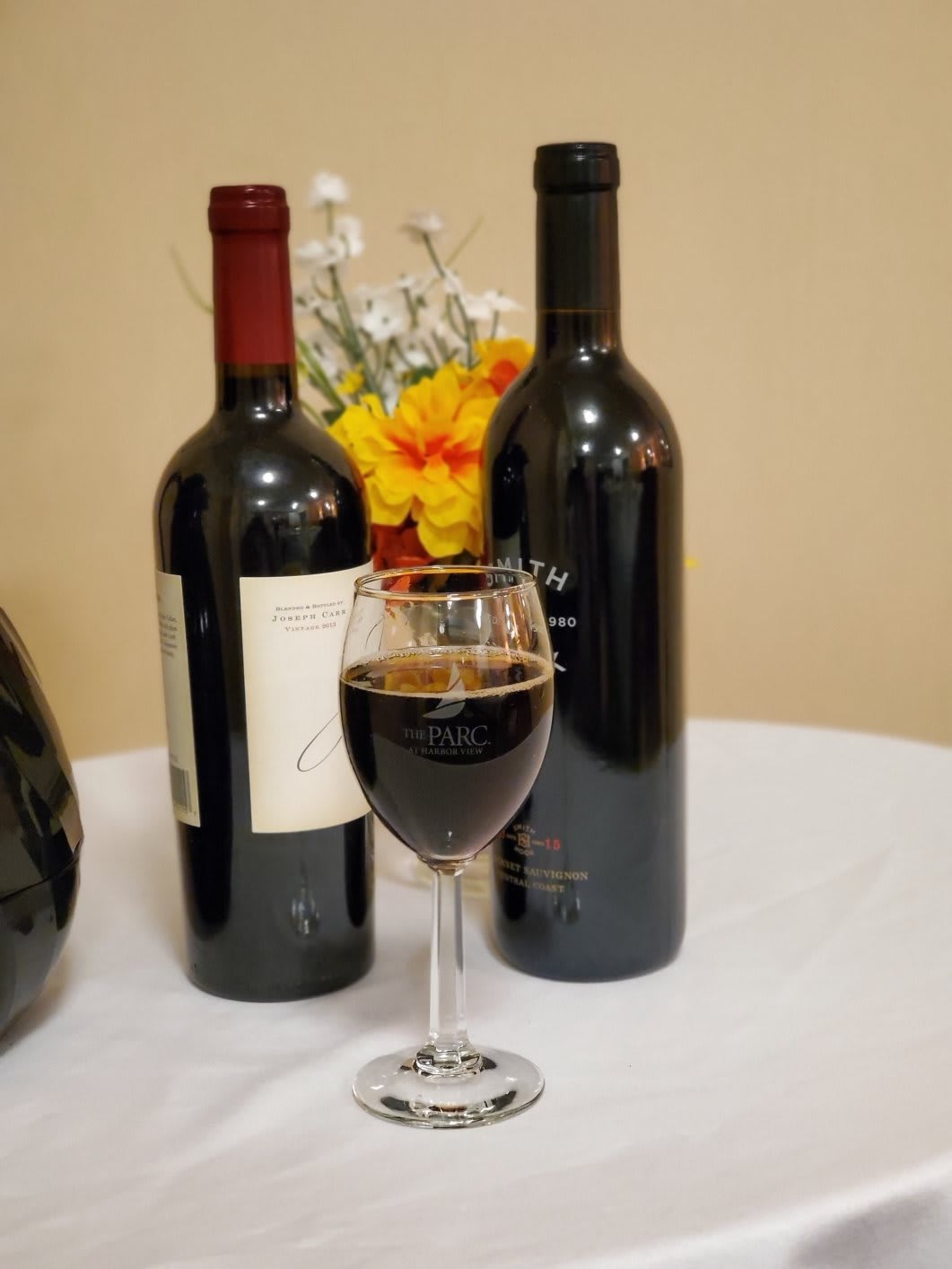 A glass of red wine surrounded by two bottles on a table adorned with flowers.