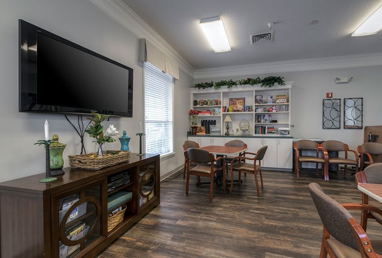 A cozy living room with a television, bookshelves, and a round table surrounded by chairs.