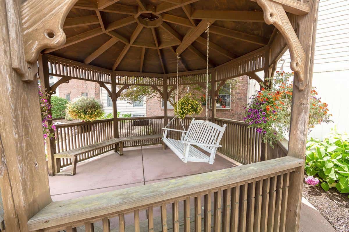A wooden gazebo with a white swing and hanging plants.