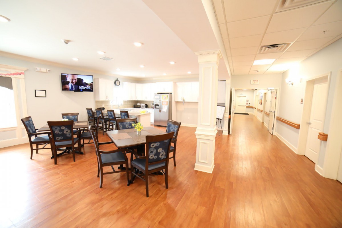 A bright dining area with wooden flooring, featuring tables and chairs alongside a modern kitchen.