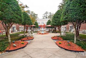 A beautifully landscaped garden with a symmetrical design featuring trimmed trees and colorful flowerbeds lining a central pathway.