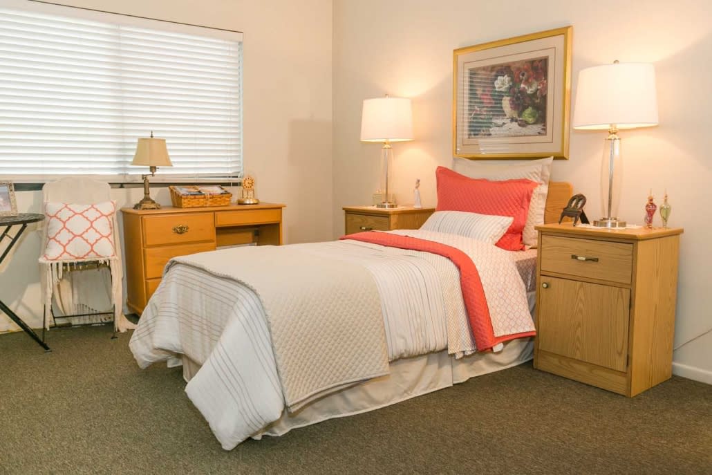 A cozy bedroom with a neatly made bed, surrounded by wooden furniture and soft lighting.