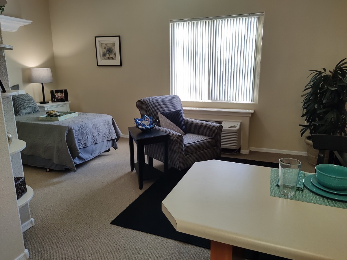 A cozy bedroom with a bed, armchair, and table near a window.