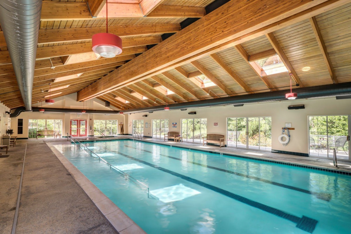 A spacious indoor swimming pool with a wooden ceiling and ample natural light streaming through skylights and large windows.