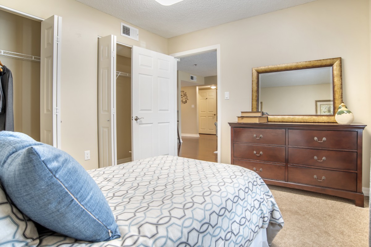 A cozy bedroom with a neatly made bed, wooden dresser, and mirror.