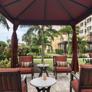 A cozy outdoor gazebo area with seating, surrounded by lush gardens and palm trees.