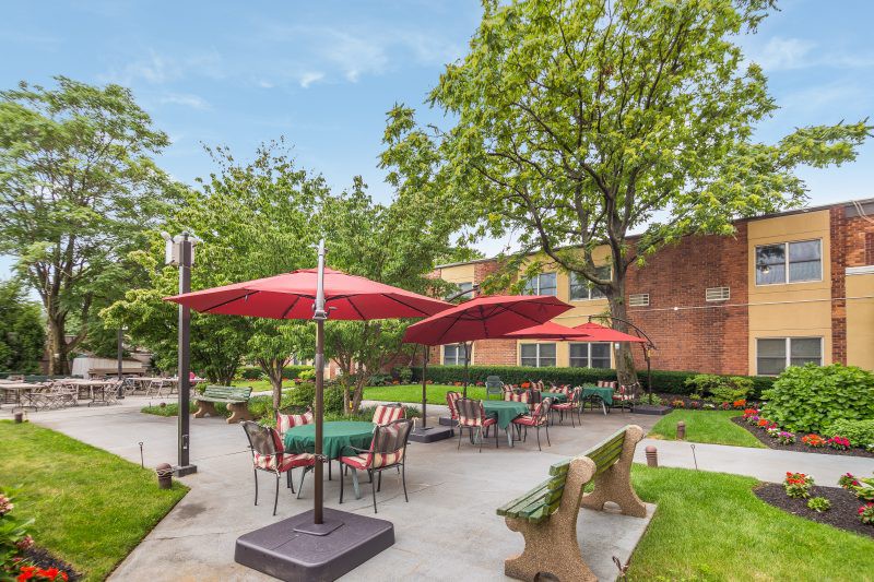 An inviting outdoor patio area with tables, chairs, and umbrellas surrounded by greenery.