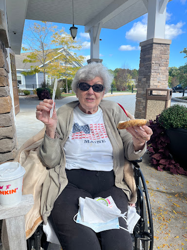 An elderly woman enjoying a snack outdoors on a sunny day.