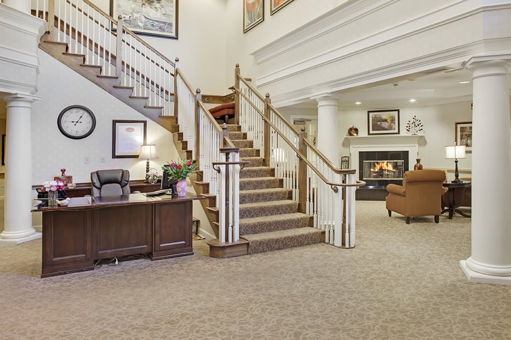 A spacious lobby area with a grand staircase, reception desk, and comfortable seating by the fireplace.