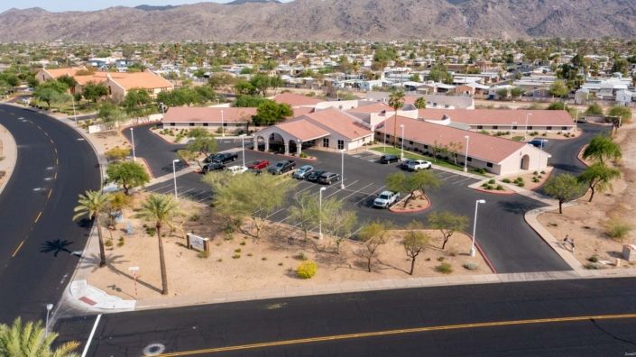 Aerial view of a building surrounded by a desert landscape with mountains in the background and a parking lot in front.