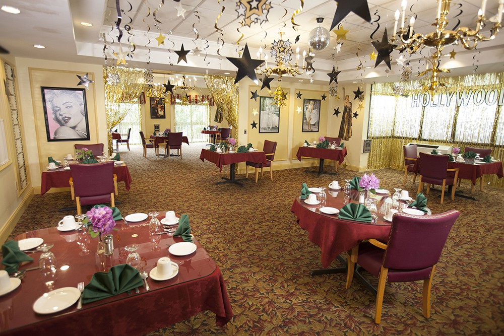 A festively decorated dining room with tables set and chandeliers hanging from the ceiling.