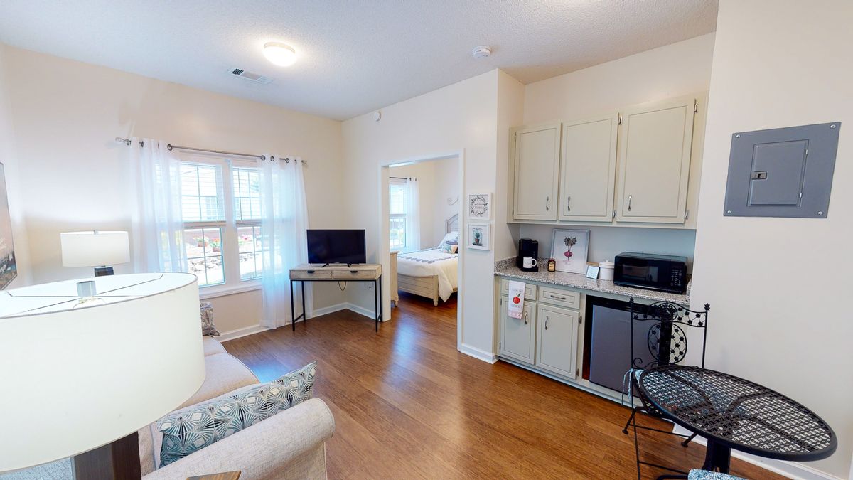 A cozy apartment with a living area and kitchenette, featuring a television and large windows.