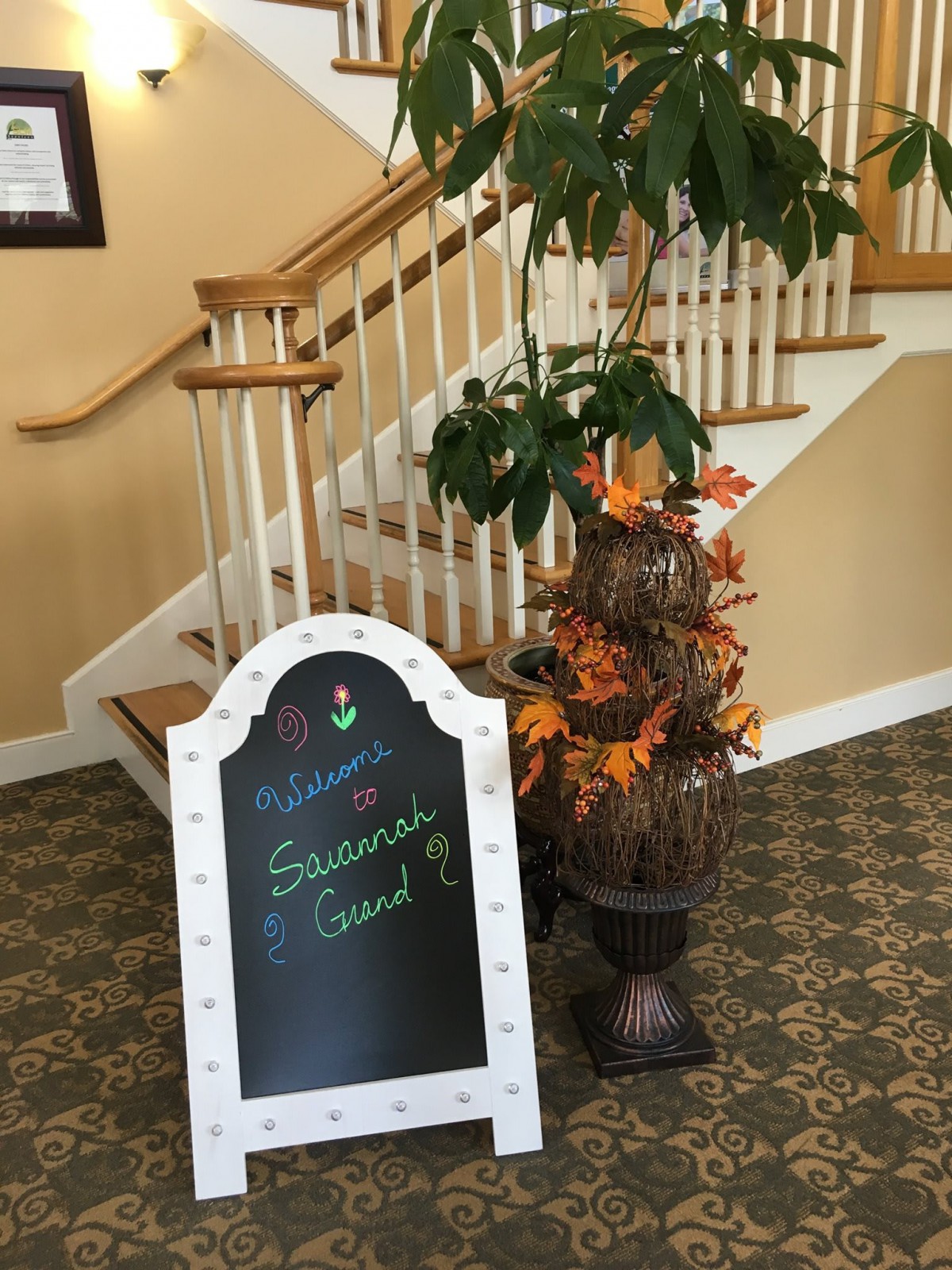 A welcoming autumn-themed sign next to a staircase with plants and seasonal decorations.