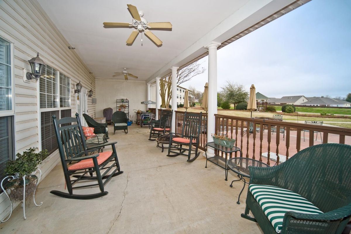 A spacious covered porch with several rocking chairs and a ceiling fan, providing a cozy outdoor seating area.