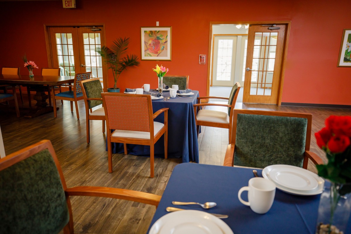A cozy dining area with neatly set tables and warm orange walls.