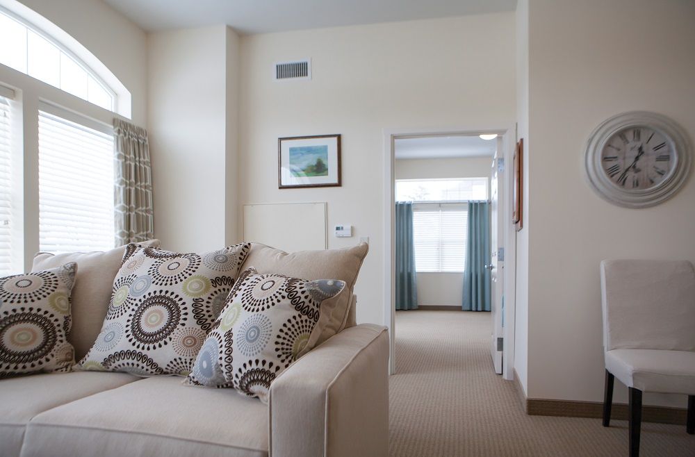 A cozy living room featuring a sofa with decorative pillows, leading to another room through an open doorway.