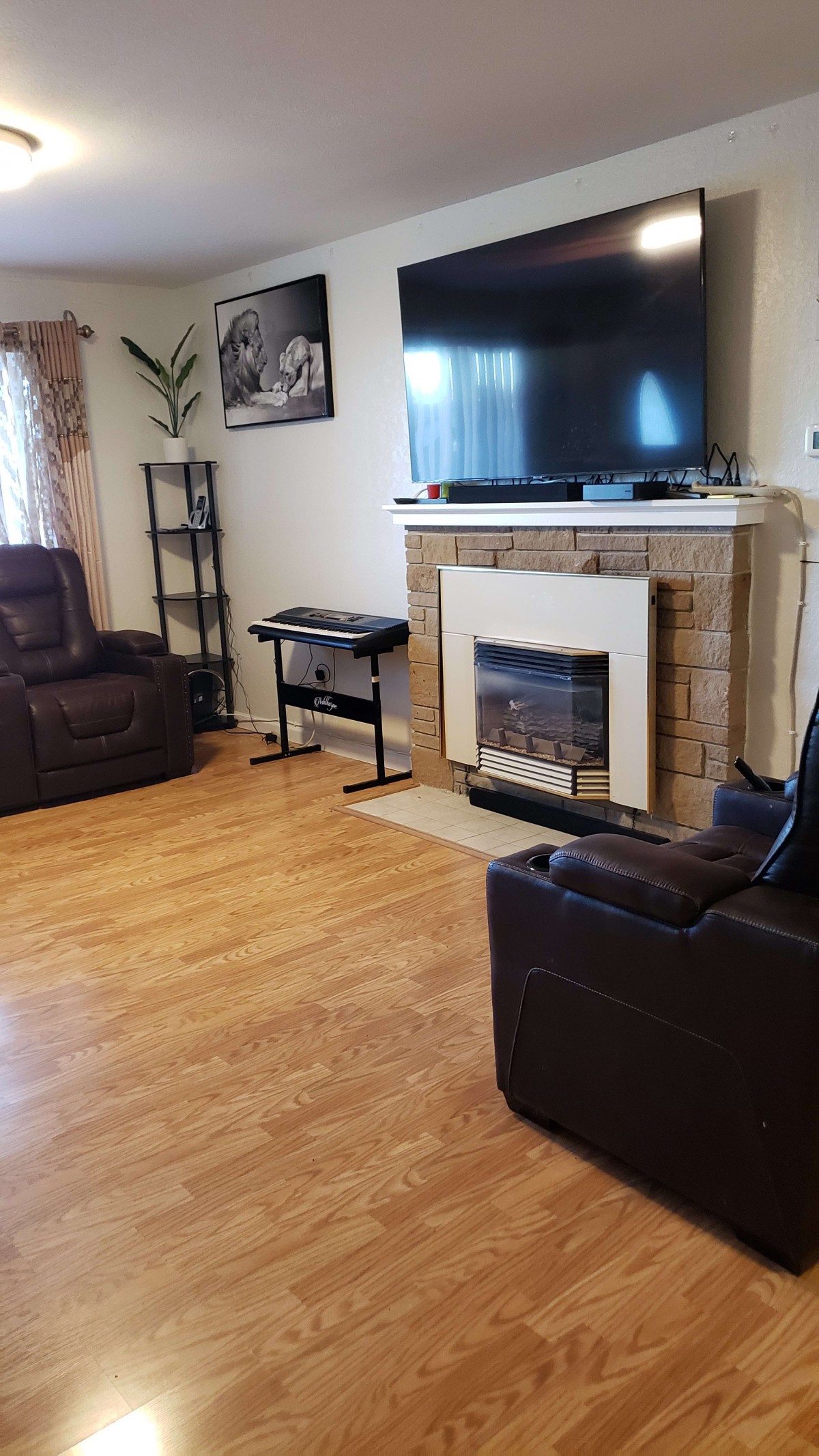 A cozy living room with recliner chairs, a television above a fireplace, and hardwood flooring.