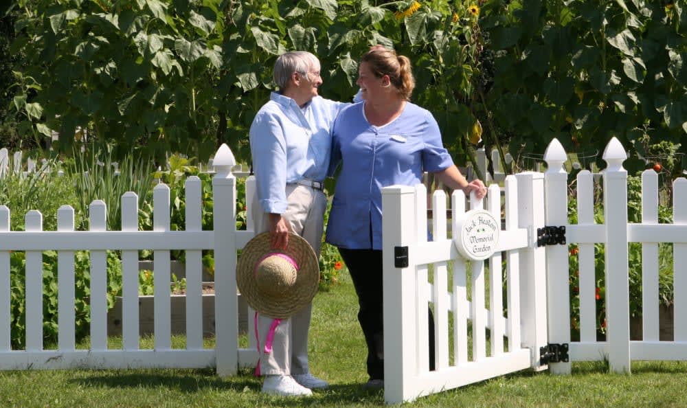 Two women enjoying time together in a garden by a white picket fence.
