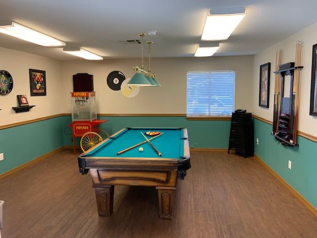A cozy billiards room featuring a pool table with cue sticks and balls, an arcade game, and decorative posters on the walls.