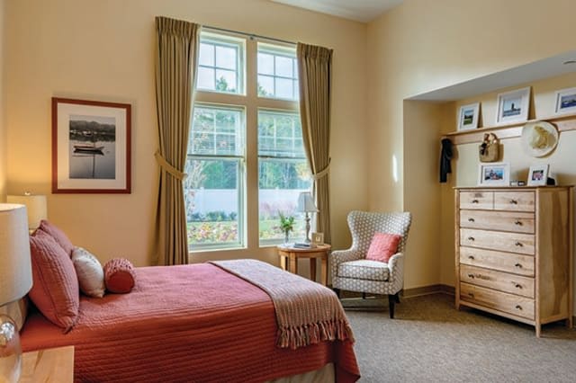 A cozy bedroom with a large window, comfortable armchair, and neatly made bed.