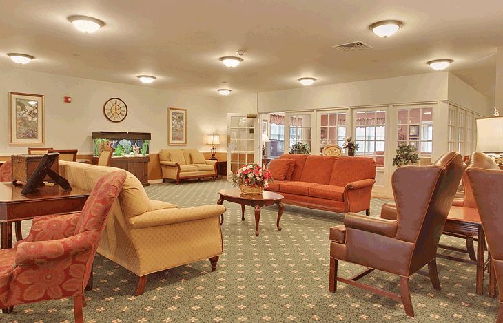 A cozy living room area featuring several sofas, armchairs, and a central wooden coffee table on a patterned carpet.