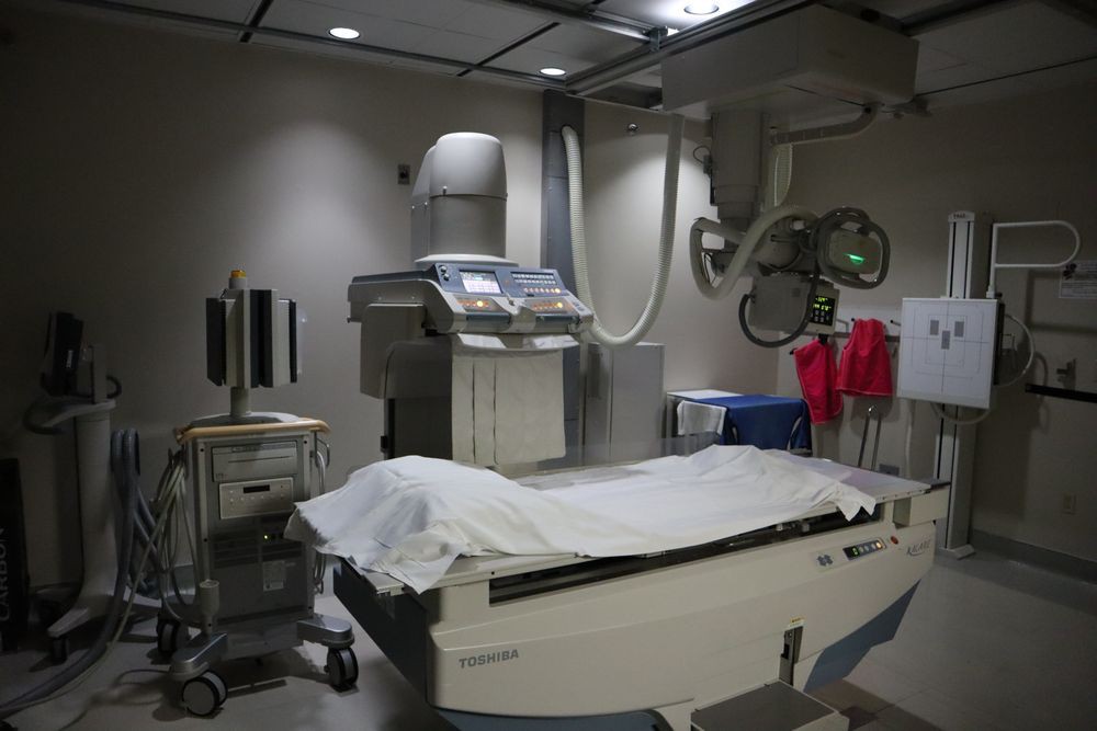 A hospital examination room featuring an X-ray machine and a bed.