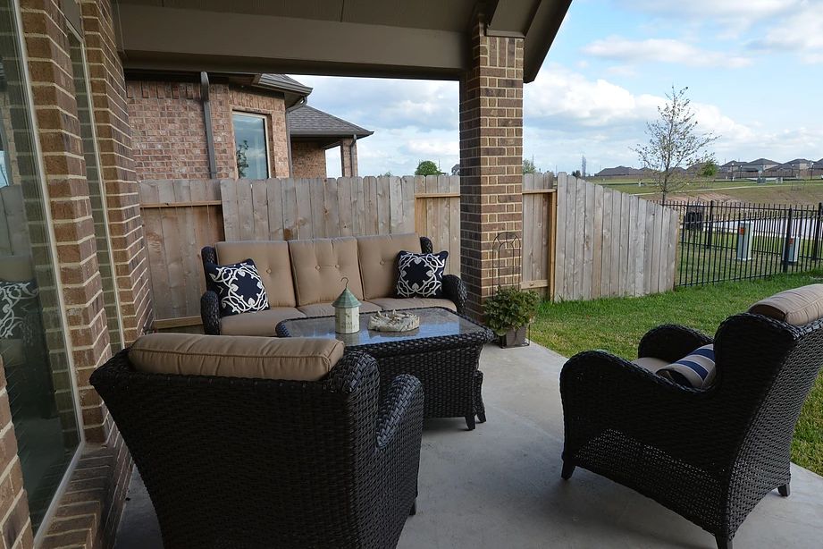 A cozy outdoor patio setup with furniture, including a couch and chairs, next to a wooden fence and brick house.