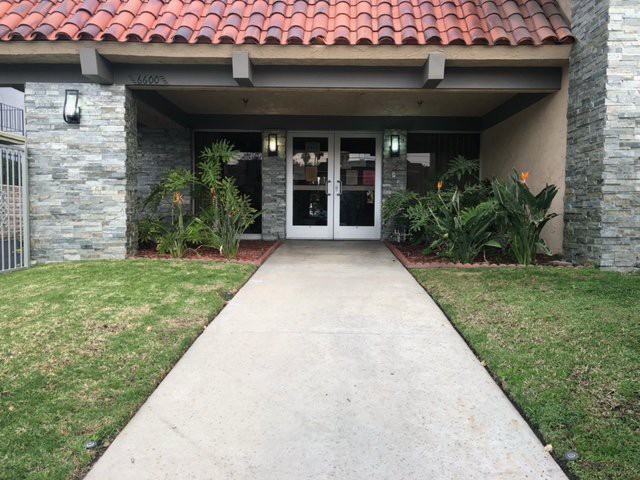 A building entrance with a concrete pathway and surrounding plants.