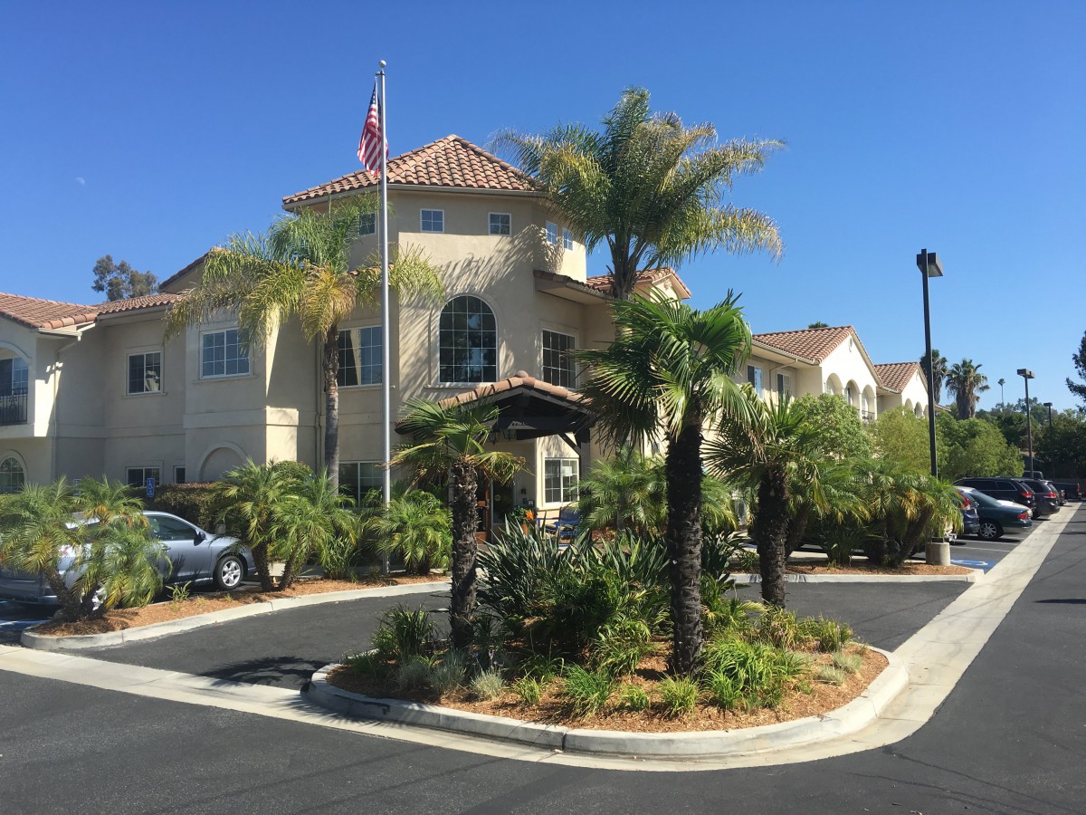 A residential building surrounded by palm trees and landscaping, with an American flag displayed at the entrance.
