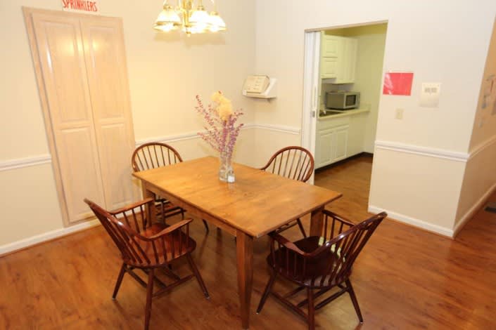 A cozy dining room with a wooden table and chairs, featuring a chandelier and an adjacent kitchen.