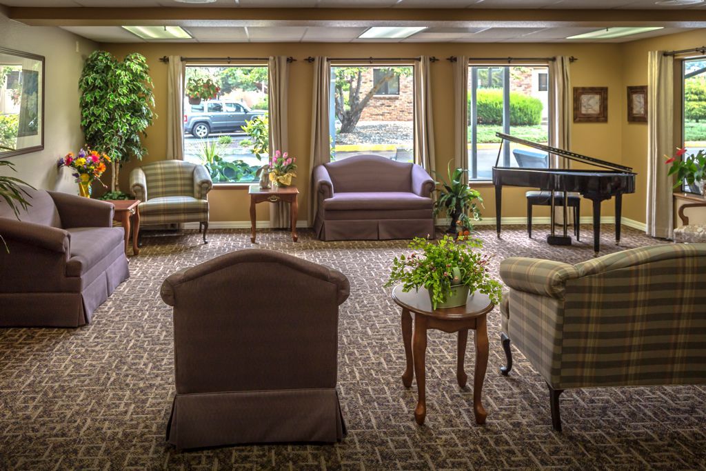 A cozy living room with comfortable seating and a piano by large windows.