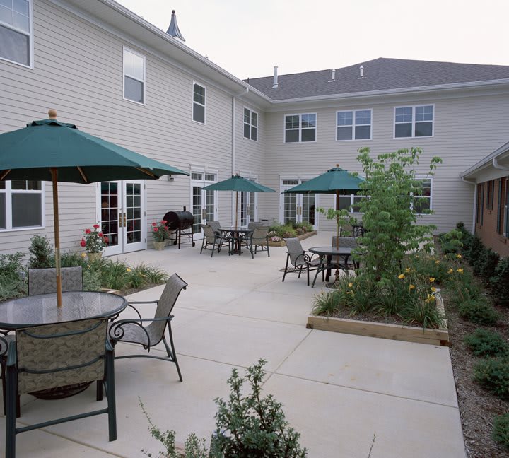 A spacious patio area with tables, chairs, and green umbrellas outside a residential building.