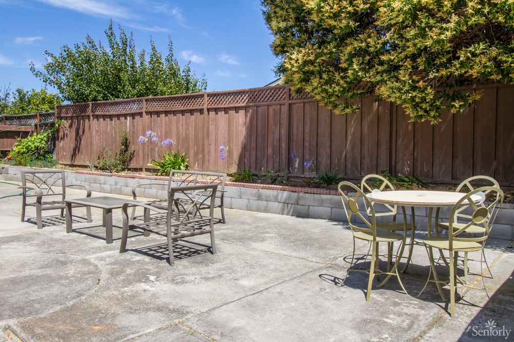 A sunny patio with outdoor seating surrounded by a wooden fence and greenery.