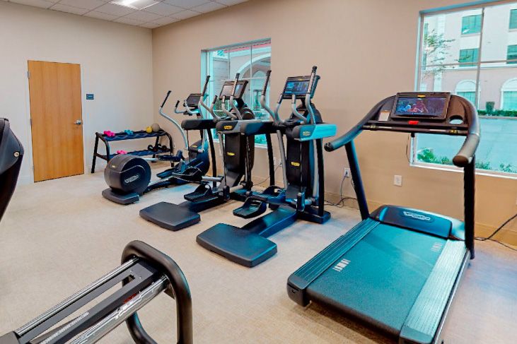 A modern gym with various exercise equipment including treadmills, ellipticals, and stationary bikes.