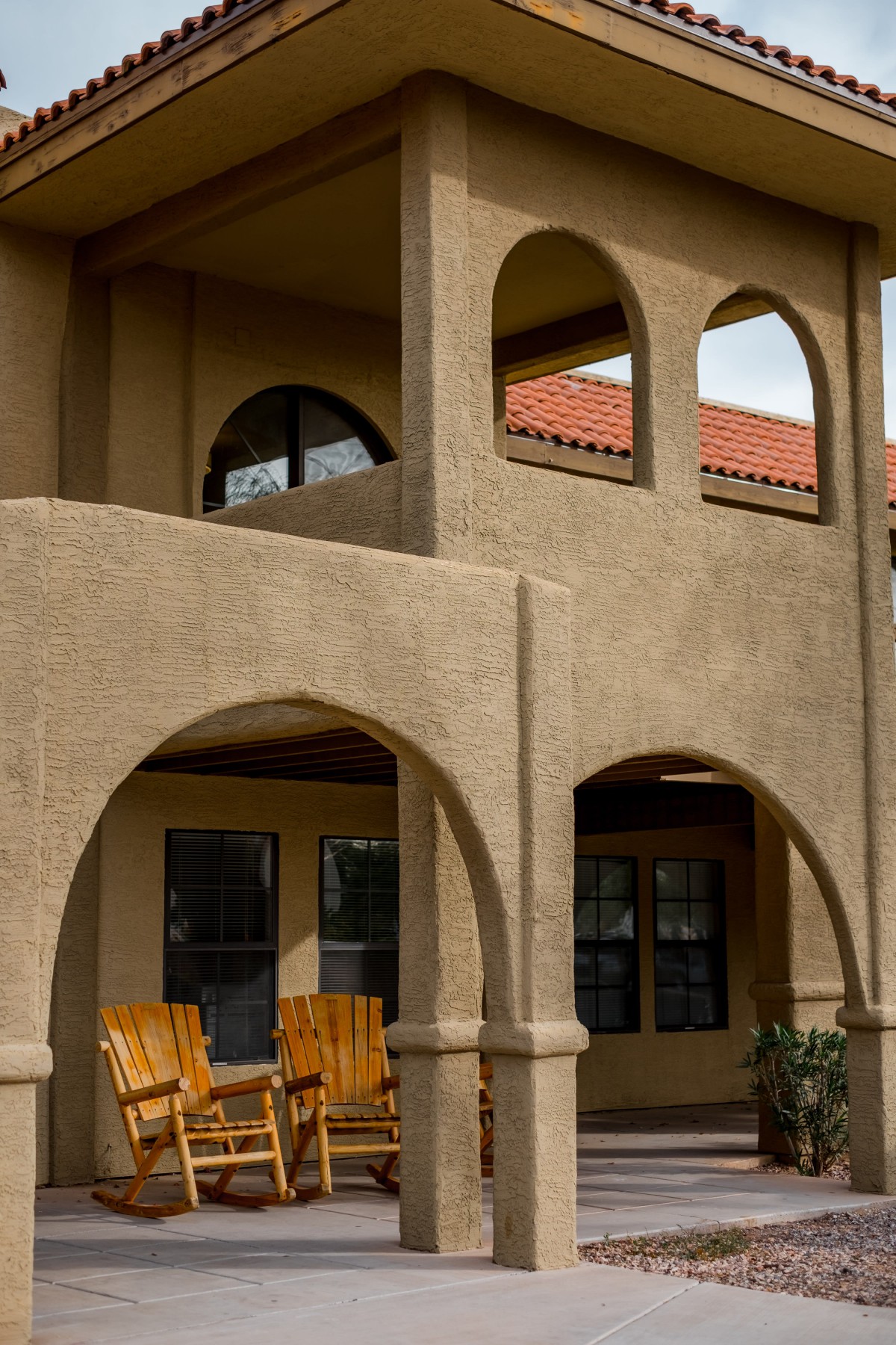 A stucco house with arched balconies and wooden patio chairs.