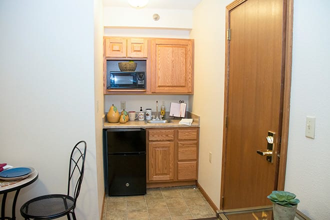 A small kitchenette with a microwave, mini fridge, and wooden cabinets.