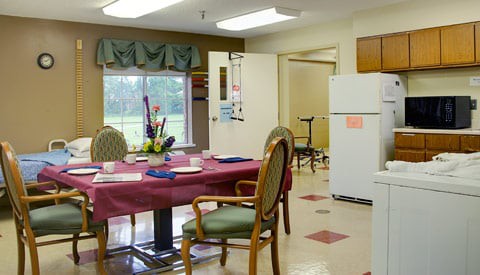 A cozy dining area with a table set for meals, surrounded by chairs, and a refrigerator in the background.