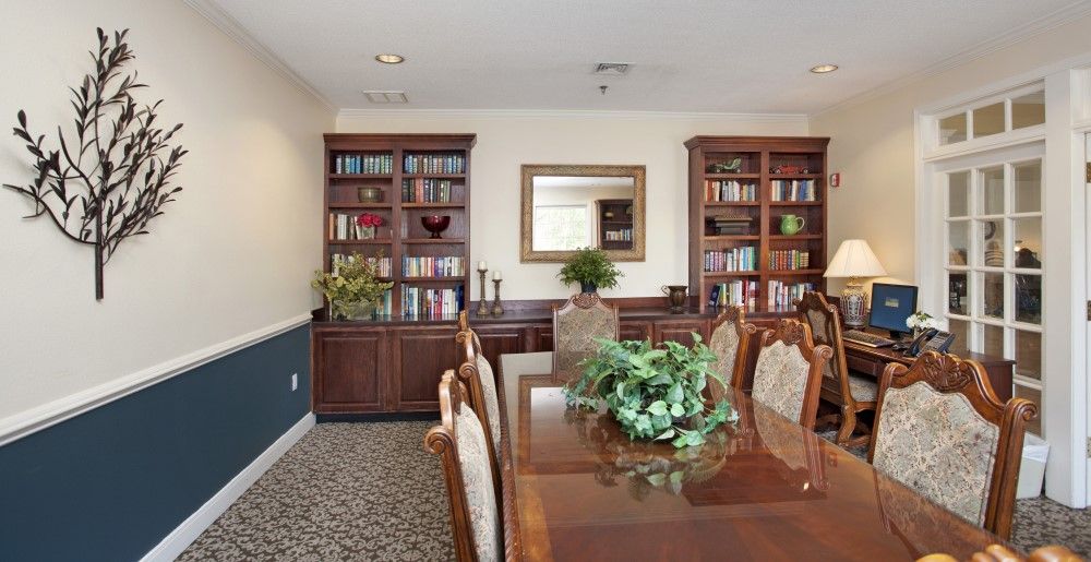 A well-furnished dining room with bookshelves, a large table, chairs, and decorative plants.