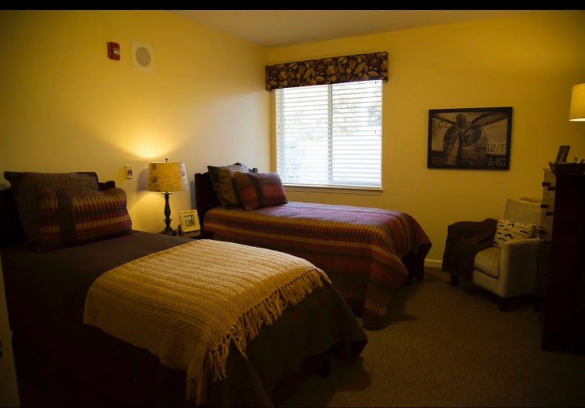 A cozy bedroom with twin beds, a lamp, and an armchair near the window.
