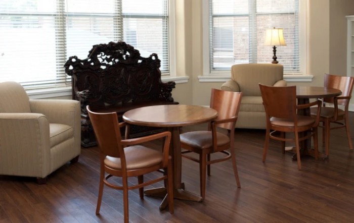A cozy living room with a wooden table and chairs, surrounded by sofas and a decorative lamp.