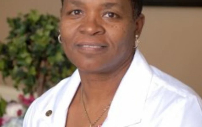 A woman in professional attire, wearing a white coat.