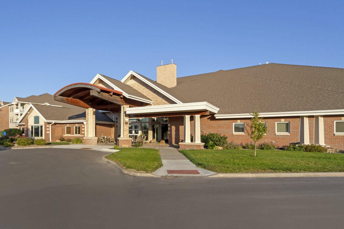 A brick building with a covered entrance and a landscaped driveway under a clear blue sky.