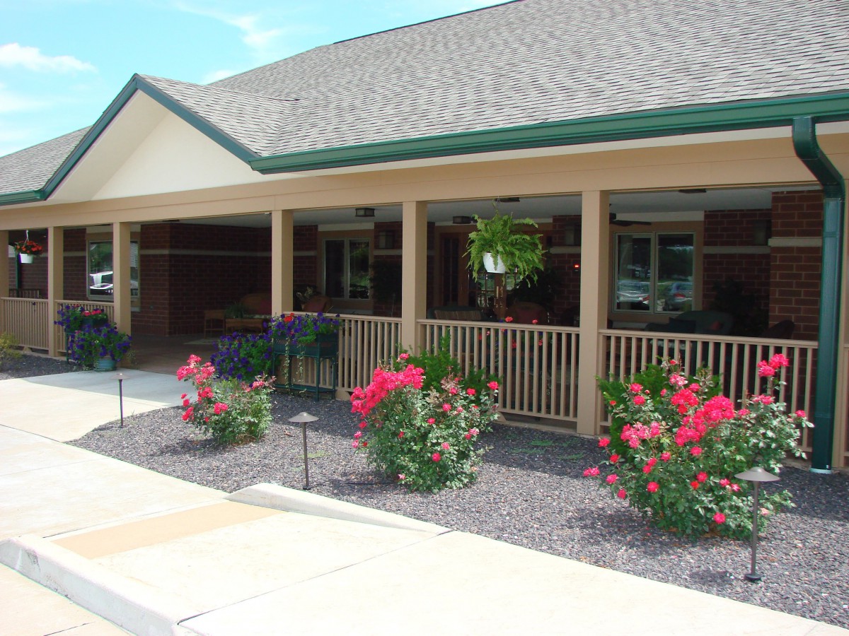 A building with a porch and a garden of colorful flowers in front.