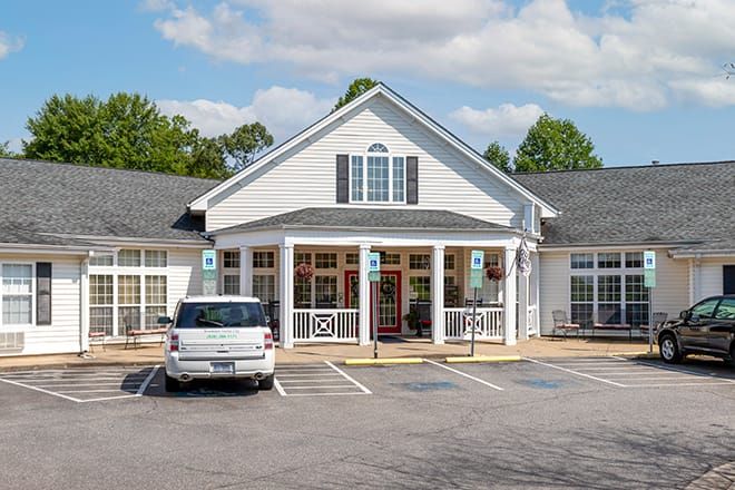 A white traditional-style building with a parking lot in front, under a partly cloudy sky.