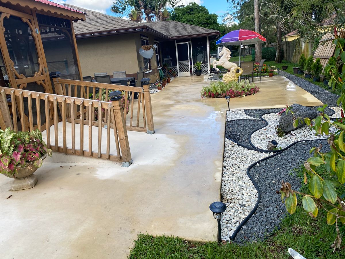 A backyard patio with a ramp leading to a garden area, featuring decorative landscaping and outdoor seating under a colorful umbrella.